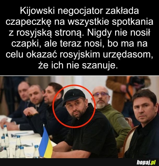 Nie wstaje z krzesła i trzyma ręce w kieszeni.